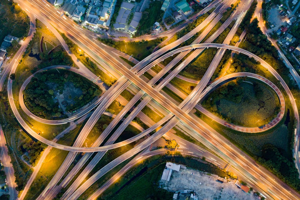 Aerial view of a highway intersection illuminated at night, showcasing the flow of traffic and surrounding city lights.